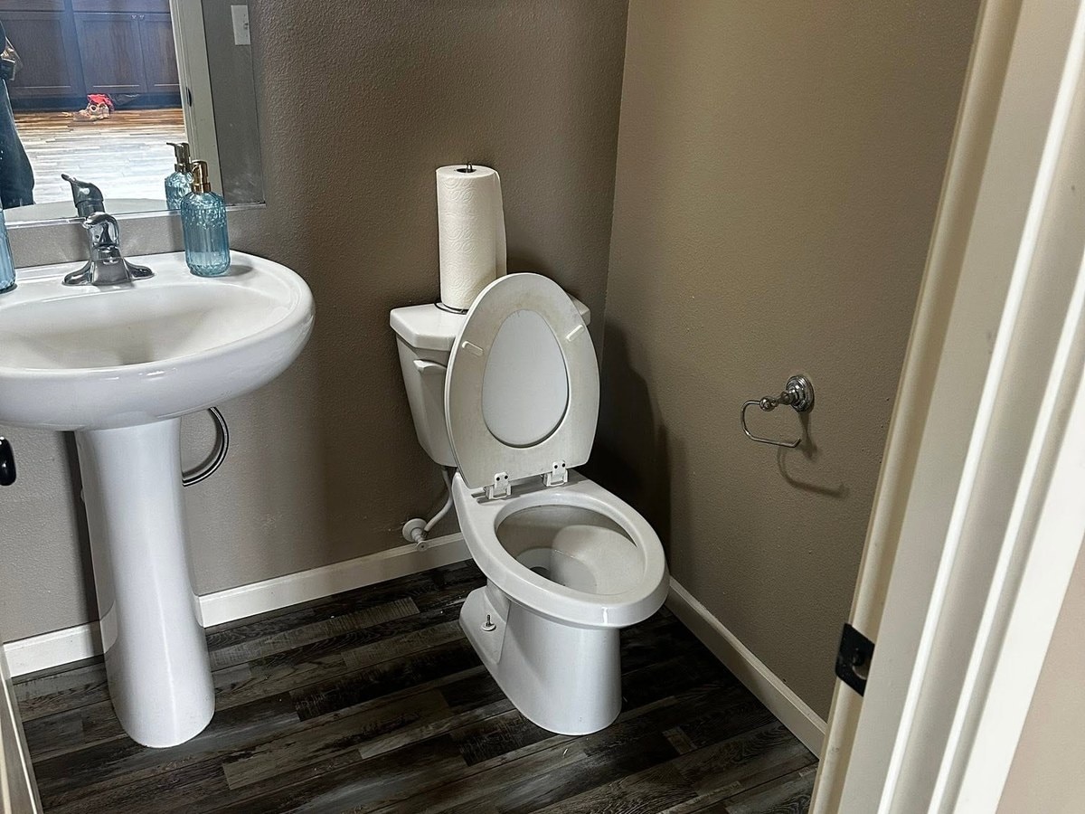 The same bathroom finished with a pedestal sink, toilet and grey plank flooring