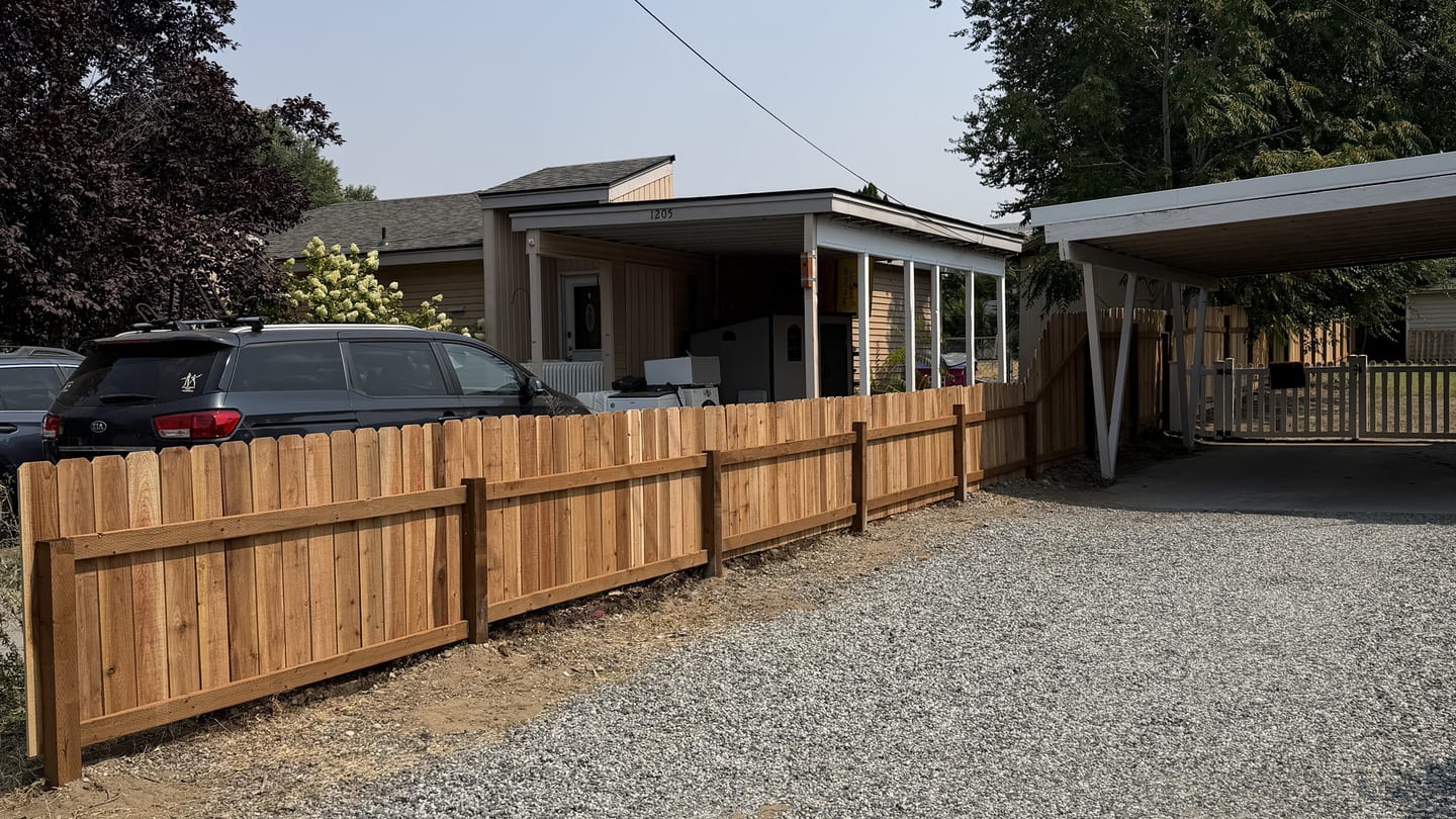 New cedar fence running along a gravel driveway