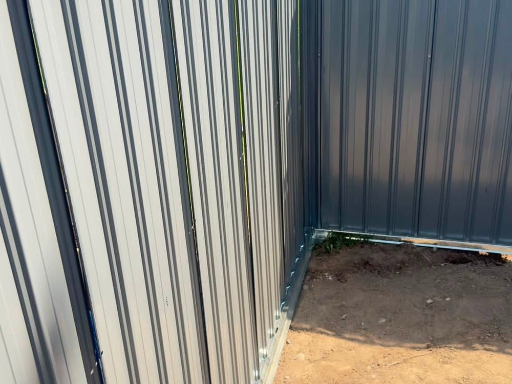 Corrugated steel wall panels meeting at a corner above bare dirt inside the structure