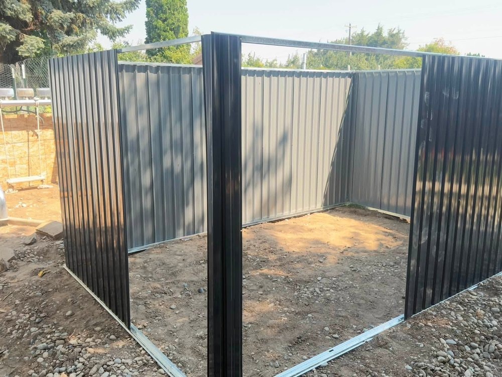 Corrugated steel walls set up on bare dirt with the roof frame still open