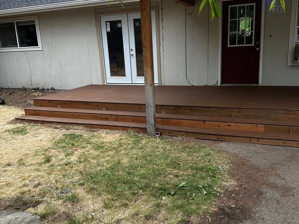 The finished deck and its two steps running past the support post, seen through leafy branches