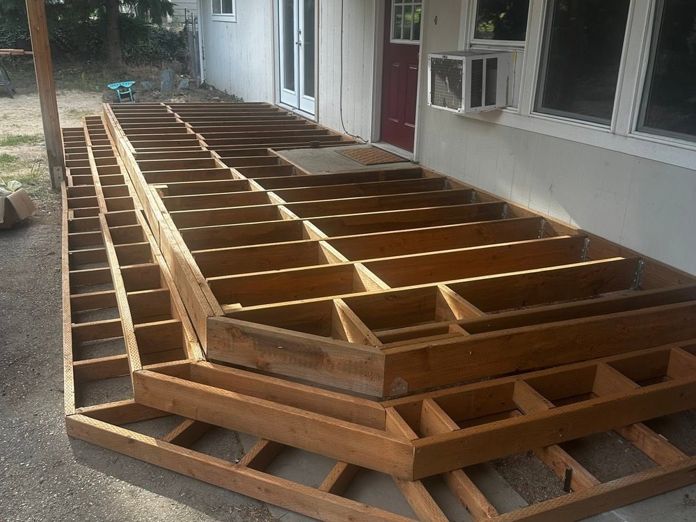 Deck joist framing and stepped tiers running alongside the house under the covered overhang
