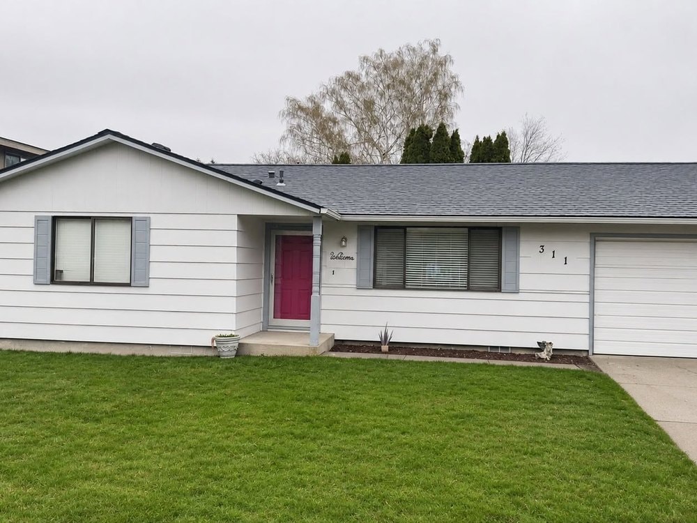 White siding with gray shutters and a white garage door, pink front door at the center