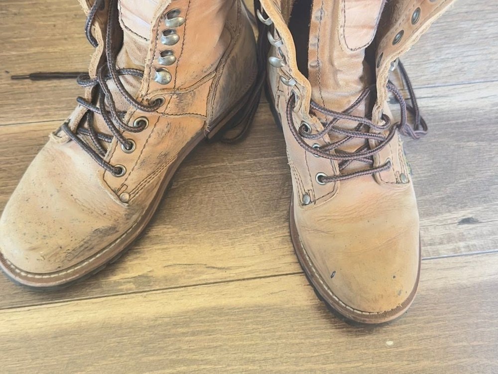 A worn pair of tan leather work boots with loosened laces on a wood floor