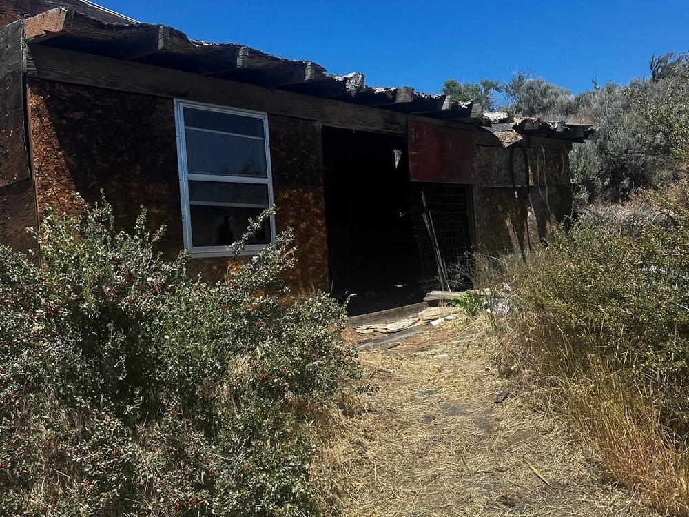 The open doorway of the original building, with sagebrush grown up against the wall