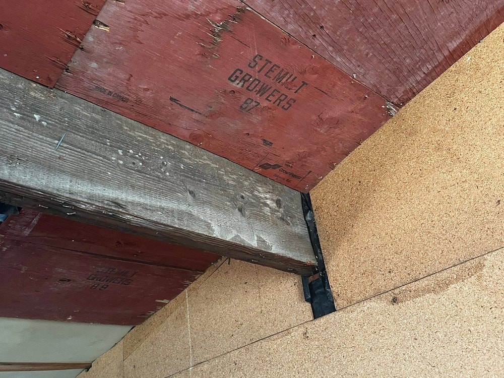 Interior before work: red painted ceiling boards, an exposed beam, and bare particle board walls