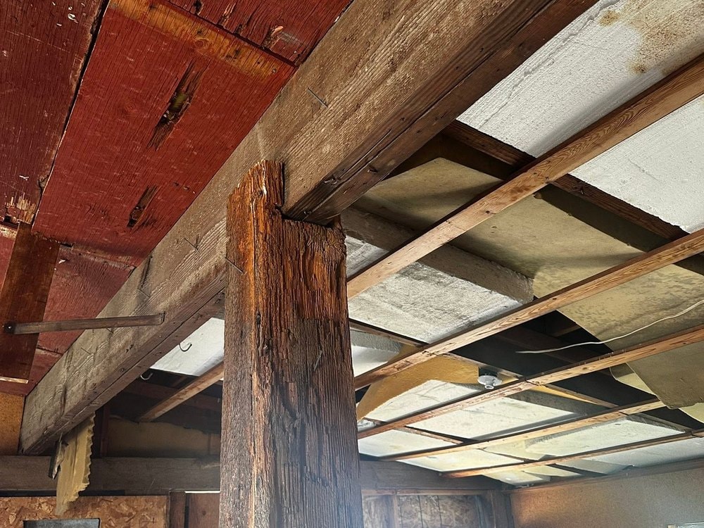 Interior before work: rough timber post and open joists under the red ceiling