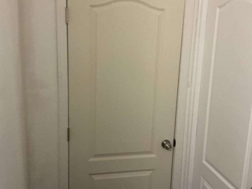 Close view of the closed white arch top panel door and its knob beside a matching door