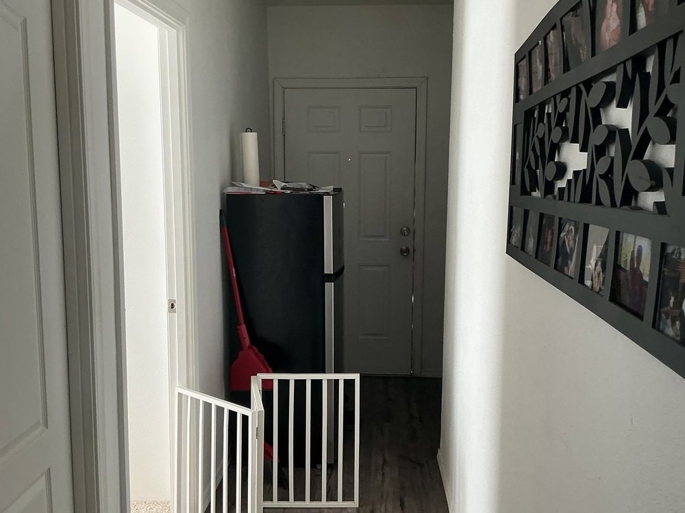 Hallway with a doorless opening into a carpeted room, a folding pet gate, and a black refrigerator
