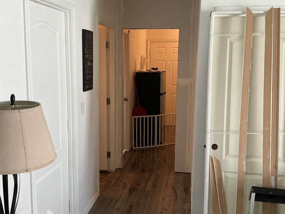 Unfinished drywalled opening framed across the hallway, with a white door slab and bare boards leaning nearby