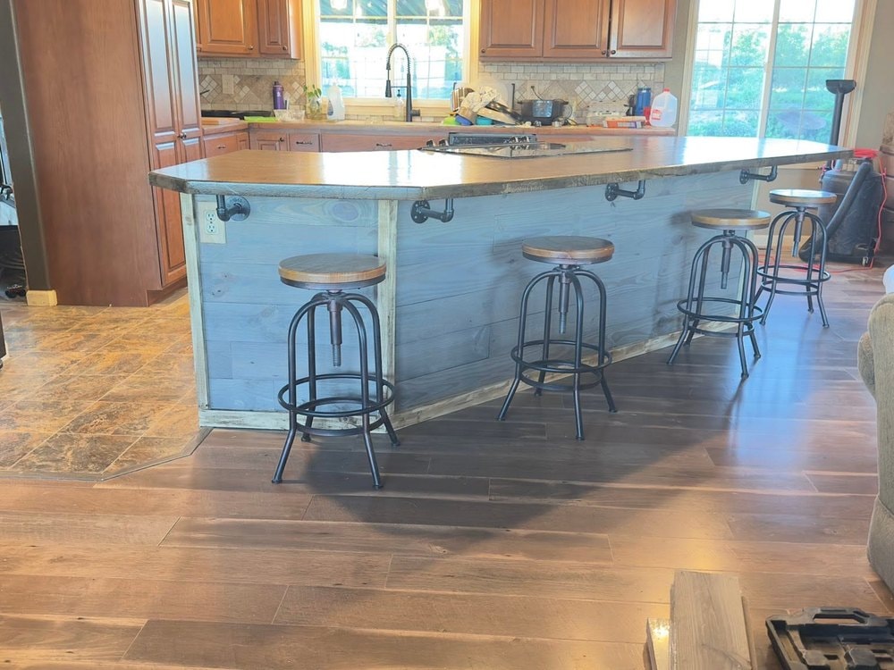 The lowered island with grey plank front and four stools, seen across the room