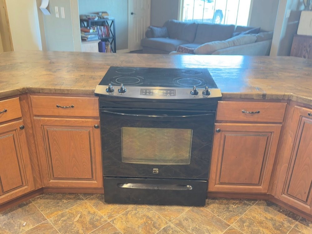 Black range in the island with the old mottled tan counter running flat across, living room beyond
