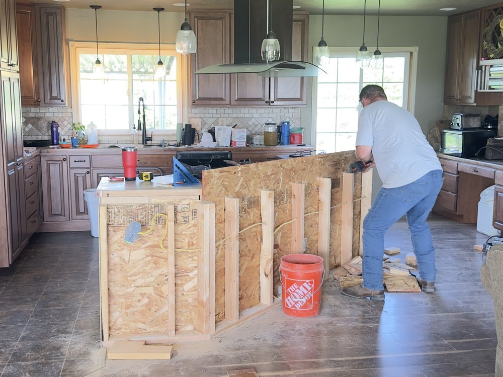 Someone driving a screw into the sheathed island framing with a cordless drill