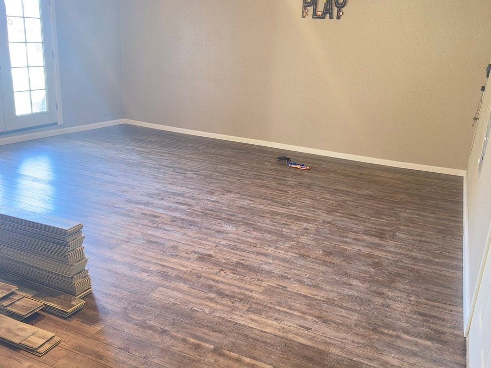 Empty room with new plank flooring and baseboard, leftover planks stacked beside the glass doors