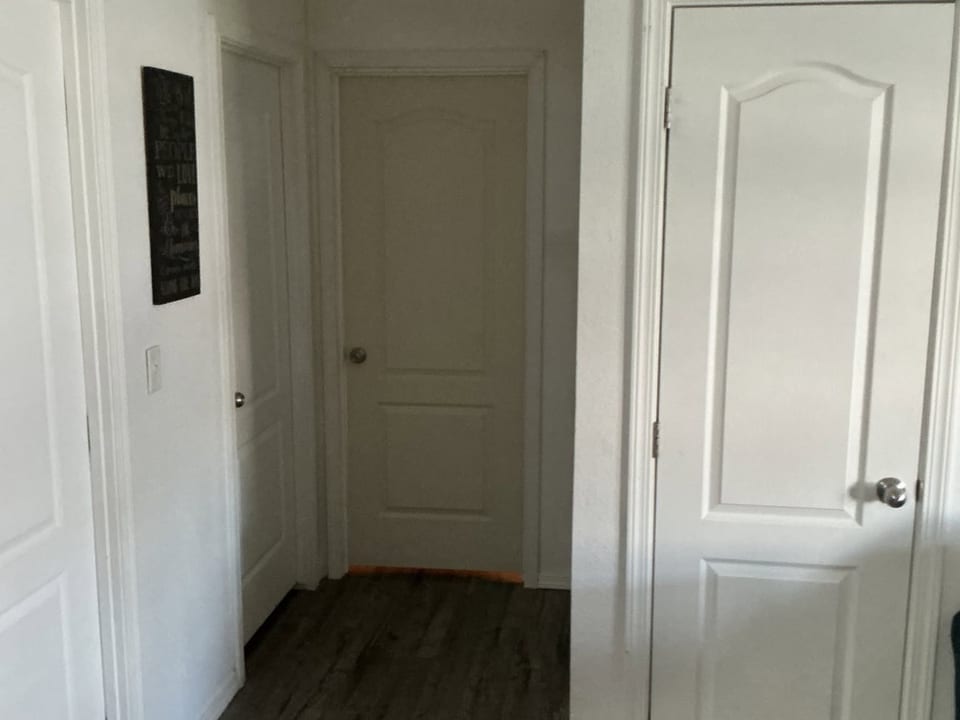 White raised panel doors line a narrow hallway with dark plank flooring and a small framed wall sign.
