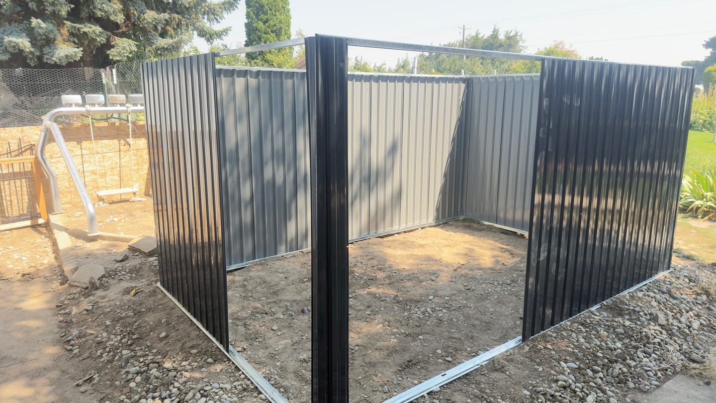 Finished corrugated metal fence enclosing a corner of a rural yard