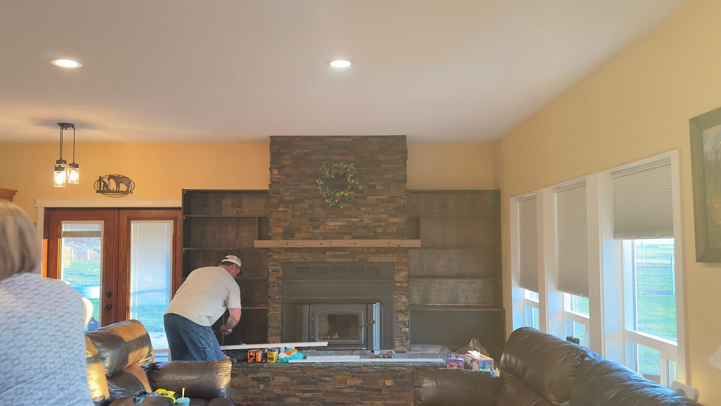 Dark wood built-in shelving going in beside the stone fireplace